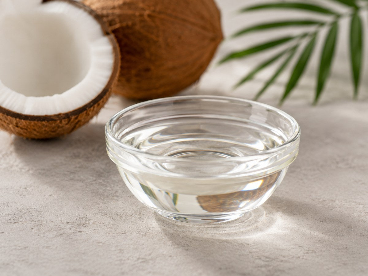 A bowl of MCT oil beside a halved coconut